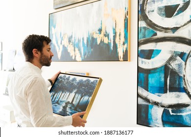 Good-looking adult artist in his 30s is about to hang a colorful little painting in the wall of an art gallery  - Shutterstock ID 1887136177