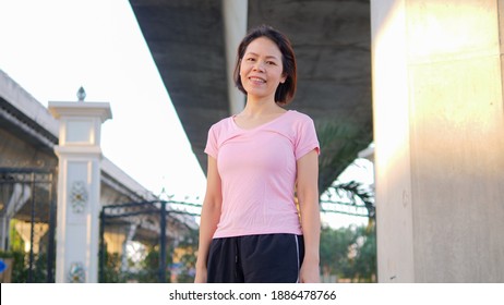 A Good-looking Asian Middle-aged Woman With Short Black Hair Happily Smiles At The Camera. Healthy And Beautiful Woman Getting Ready To Exercise In The Morning Where The Morning Sun Shines Down