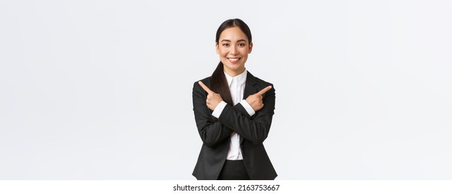 Good-looking asian saleswoman suggest two choices. Attractive businesswoman in black suit pointing fingers sideways, have few variants, help make decision, standing white background - Shutterstock ID 2163753667