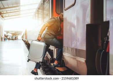 Good-looking Bearded Black Man Boarding A Train. African Businessman On The Railway Station With A Gray Suitcase And In Social Clothes: Leather Shoes, Short Sleeve Suit, And Watch; Business Trip