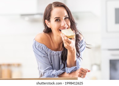 Good-looking girl bites off the slice of bread with a white spread.