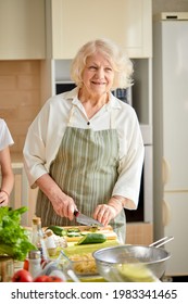 Good-looking Gray-haired Lady In Apron During Cooking In Kitchen At Home, Smiling, Enjoy Culinary Time, Posing, Alone. Cute Grandma Standing Next To Table, Shining With Happiness