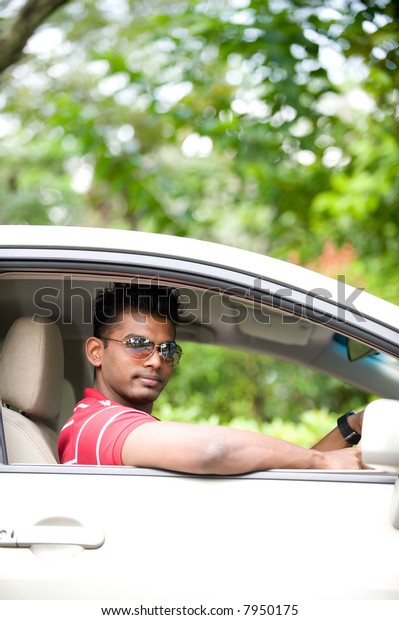A good-looking Indian man in sunglasses\
sitting in drivers seat of car\
outside