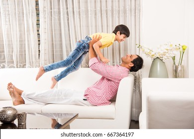 Goodlooking Indian/Asian Playful Father Son Having Good Time At Home While Sitting Over Sofa