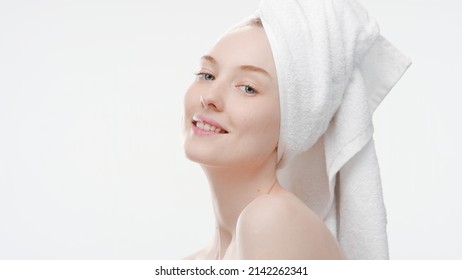 Good-looking slim European young woman with a hair towel on her head tilts her head back smiling wide for the camera on white background | Skin care concept