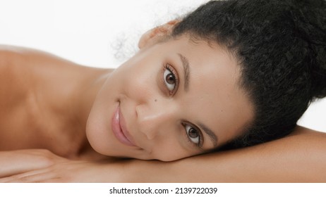Good-looking slim young African American woman lays her head on her forearm and smiles for the camera on white background | Flawless skin, beauty care concept