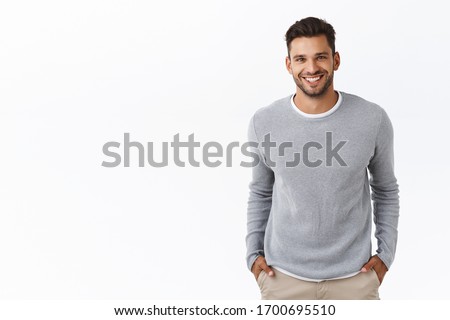 Good-looking stylish modern hispanic guy with stylish haircut, beard, wear grey sweater over t-shirt, hold hands in pockets and smiling joyfully, laughing chatting with friends, white background