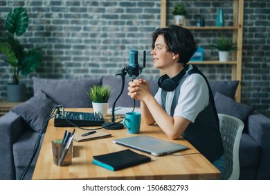 Good-looking teenager speaking in microphone in sound recording studio sitting at desk alone using modern equipment. Audio podcasts and adolescence concept.