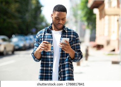 Good-looking Young Black Hipster Messaging Online On His Cell Phone, Walking Down The Street With Coffee Cup