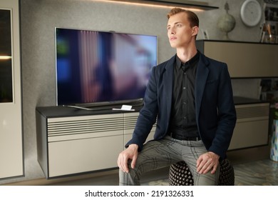 A Good-looking Young Businessman In A Smart Suit Sitting In A Modern Apartment. Interior And Furniture For Office And Home.