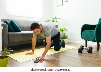Good-looking Young Latin Man Using The Stopwatch On A Smartphone To Start His Home Workout In The Living Room