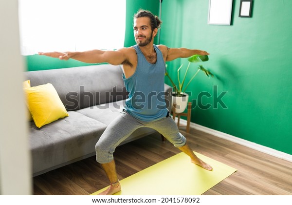 Good-looking young\
man practicing a warrior yoga pose in his living room. Active man\
working out with a yoga\
routine