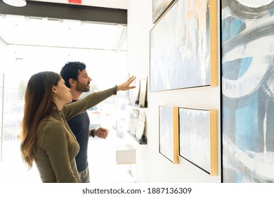 Good-looking Young Woman And Adult Man Are Deciding Which Art Painting To Buy For Their Home From The Exhibition