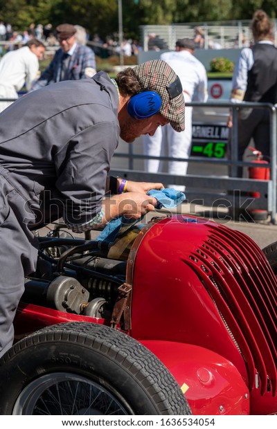 Goodwood, Sussex / UK - 13 Sept 2019: An engineer\
with ear defenders, tweed cap and blue polishing cloth works on a\
red 1935 vintage V8R1 Maserati at Revival.The hood is off exposing\
the engine.