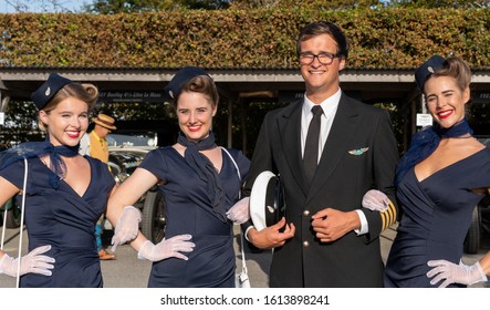 Goodwood, Sussex / UK - 14 Sept 2019: Three Air Hostess Pose In Retro Corporate Uniforms Alongside A Flight Captain With Suit, Tie And White Cap. Group Posed In Vintage Costumes At Sunny  Revival.