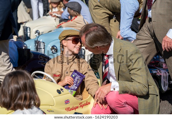Goodwood, Sussex / UK - 15 September 2019: A young\
driver with pigtails sits in a pedal car, Montague Tegerdine,\
smiling at an older man who stoops to whisper; she holds a bar of\
Cadburys Dairy Milk.