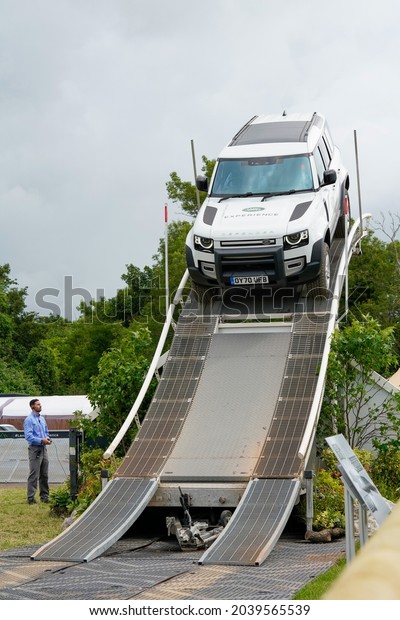 Goodwood, Sussex, UK - 8 Jul 2021: A white Landrover\
Defender navigates a steep downward slope tilted at a scary\
adrenaline-charged angle in a performance demonstration at the\
Festival of Speed. 
