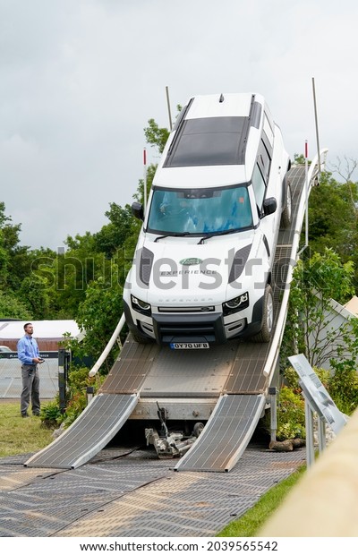 Goodwood, Sussex, UK - 8 Jul 2021: A white Landrover\
Defender navigates a steep downward slope tilted at a scary\
adrenaline-charged angle in a performance demonstration at the\
Festival of Speed. 