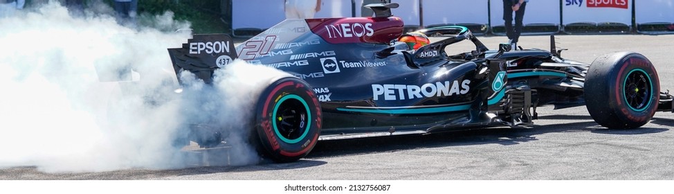 Goodwood, Sussex, UK - 9 July 2021: A Letterbox Crop Of A Mercedes Benz F1 W10 EQ Power+ Racing Car With Smoking Rear Tyres As It Burns Rubber Racing Away. Petronas And Ineos Sponsor The Race Team.