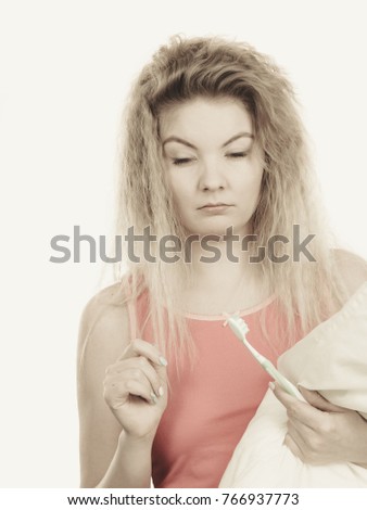 Goofy blonde woman holding toothbrush and pillow, having morning wake up trouble after big bad night.