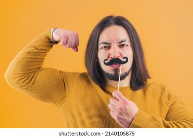 Goofy muscled caucasian man in his 30s doing silly faces and covering his face with fake moustache while looking at camera. High quality photo