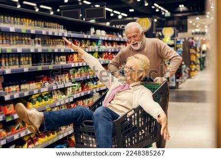 A goofy old couple is having fun with shopping cart at the supermarket.