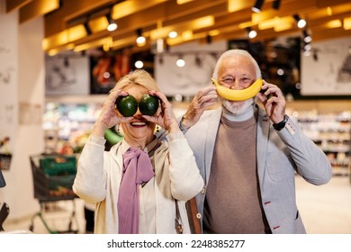 A goofy old couple is playing silly faces with fruits at supermarket. - Powered by Shutterstock