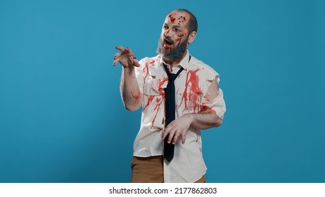 Goofy Ugly Zombie Dancing Childish On Blue Background. Creepy Mindless Brain-eating Monster With Deep And Bloody Wounds And Scars Enjoying Dance While Looking At Camera. Studio Shot