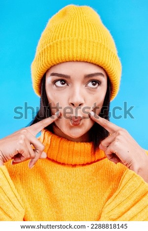 Goofy woman in winter fashion with comic expression, beanie and fun isolated on blue background. Style, happiness and silly gen z girl in studio with funny face and warm clothing for cold weather.