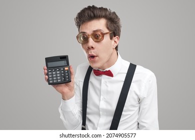 Goofy Young Man In White Shirt And Retro Glasses Demonstrating Calculator While Calculating Budget Against Gray Background