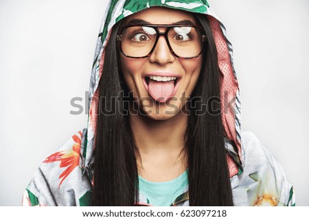 Goofy young woman wearing eyeglasses and a hooded anorak squinting and sticking out her tongue in a close up cropped head shot isolated on white