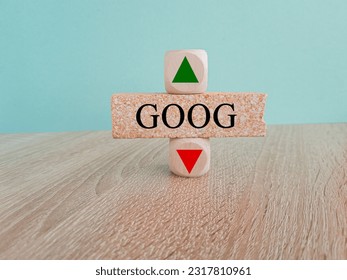 GOOG price symbol. A brick block with arrow symbolizing that GOOG index price are going down or up. Beautiful wooden table blue background. Business and gold price concept. Copy space.