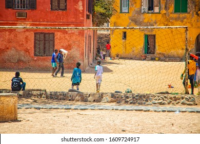 Goree Island, Senegal- April 22 2019: Unidentified Boys Play Soccer On The Sand In The Town In Africa. Boys Playing In Front Of An Old Yellow House On A Football Field. It's A Beautiful Sun Day.