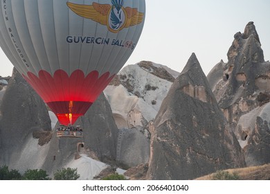 GOREME, TURKEY - AUGUST 5, 2021: Hot air balloon with tourists firing up its burner flame and flying low next to fairy chimneys cave houses in Cappadocia valley in the morning