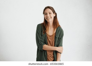 Gorgeours young European woman with healthy clean skin and beautiful set of features, dressed in dark-green shirt over brown top, wearing her hair loose, looking at camera with shy charming smile