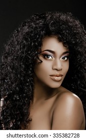 Gorgeous African Girl, With Long Black Curly Hair And Sensitive Make-up, Posing On The Black Background And Looking At Camera, Close Up