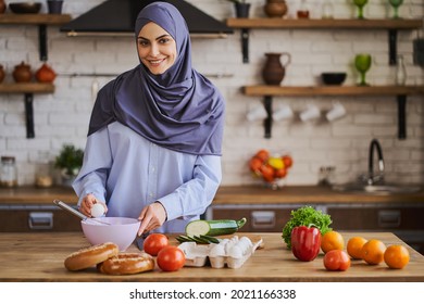 Gorgeous Arabian woman breaking the egg to whip it in a bowl. Muslim girl cooking amazing dinner. Fresh ingredients on her table.