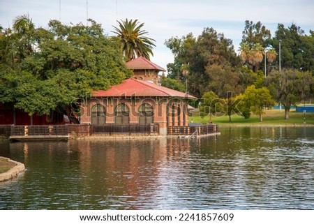 a gorgeous autumn landscape at Lincoln Park with a rippling green lake surrounded by lush green palm trees and plants, a red brick building, blue sky with clouds in Los Angeles California USA