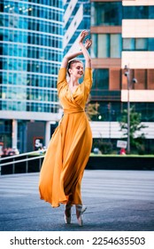 Gorgeous ballet dancer dancing on city streets background in fluttering yellow dress