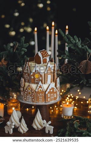 Gorgeous beautiful big homemade Christmas cake decorated with gingerbread house cookies in the living room. Festive cozy home atmosphere, lights on background, wooden table. Surprise for kids