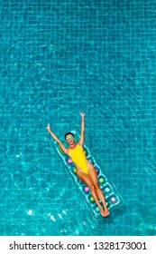 Gorgeous beautiful lady in sexy yellow bikini swims in a luxury hotel pool on an inflatable mattress. Summer holidays, travel, all inclusive. Top view on quadcopter