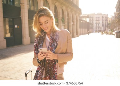 Gorgeous Beautiful Young Woman With Blonde Hair Messaging On The Smart-phone At The City Street Background. Pretty Girl Having Smart Phone Conversation In Sun Flare. 