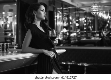 Gorgeous Beauty Young Brunette Woman In Dark Dress With Glass Of Wine Standing At The Bar In Luxury Interior