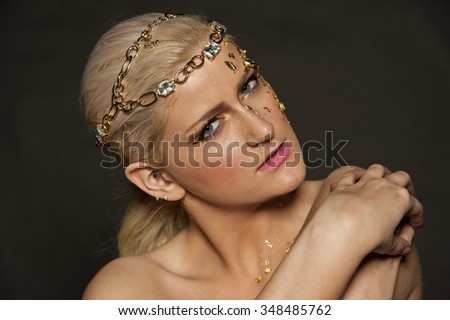 Gorgeous blond female portrait with gold flakes on her face and hair in a pony on a black background.