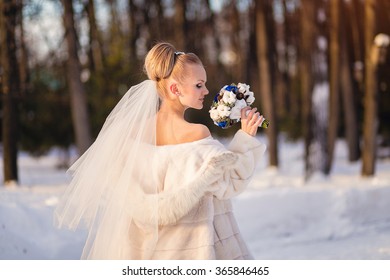 Gorgeous Blonde  Bride In Wedding Dress With Bouquet Of Blue Roses With Cotton In Winter Park.