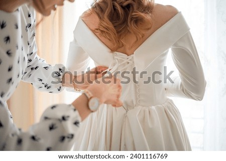 A gorgeous blonde bride in a white luxurious dress is preparing for the wedding. Morning preparation. A woman puts on a dress.