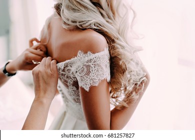 Gorgeous, blonde bride in white luxury dress is getting ready for wedding. Morning preparations. Woman putting on dress.