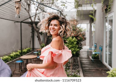 Gorgeous Blonde Girl Dancing In Outdoor Cafe. Portrait Of Amazing Smiling Woman With Tanned Skin Expressing Happiness On City Background.