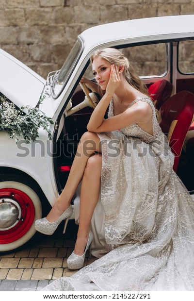 Gorgeous bride\
sitting in retro car with\
flowers