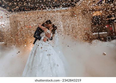 Gorgeous bride and stylish groom dancing under golden confetti at wedding reception. Happy wedding couple performing first dance in restaurant. Romantic moments - Powered by Shutterstock